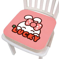 Coussin rehausseur chaise lapin épais rose avec marqué lucky dessus et un lapin caché derrière les lettres, le tout posé sur une chaise blanche et l'image sur fond blanc