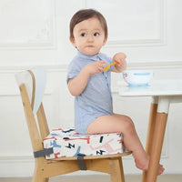 Coussin rehausseur pour enfant avec des motifs de couleur différentes. Il possède des attaches pour le fixer à une chaise pour enfant