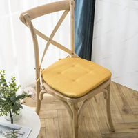 Un coussin jaune capitonné sur une chaise en bois clair posé sur un parquet