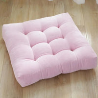 Coussin capitonné carré rose posé sur le parquet