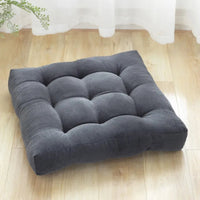 Coussin capitonné carré gris posé sur le parquet