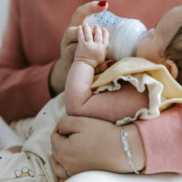 Un nourrisson buvant du lait au biberon, tendrement tenu par sa mère, avec un gros plan sur la main de bébé.