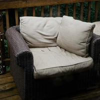 Fauteuil en osier avec coussins sur une terrasse en bois, cadre extérieur naturel.