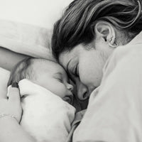 Une mère endormie en câlinant son bébé, capturant un moment tendre et intime en noir et blanc.