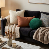 Coussins de plusieurs couleurs sur un canapé avec des plaids dans une ambience cosy