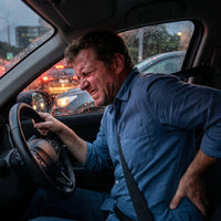 Un homme en voiture qui se tien le dos 