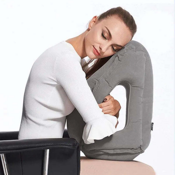 Coussin de voyage gonflable multi-positions utilisé par une femme assise que l'enlace dans ses bras et repose sa tête dessus les yeux fermés