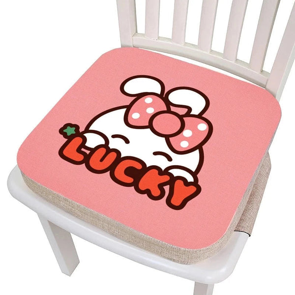 Coussin rehausseur chaise lapin épais rose avec marqué lucky dessus et un lapin caché derrière les lettres, le tout posé sur une chaise blanche et l'image sur fond blanc