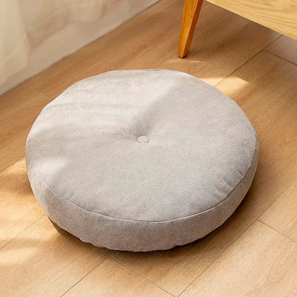 Coussin yoga pouf gris capitonné au centre il est poser au sol sur un parquet