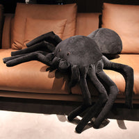 Grand coussin en forme d'araignée noire posé sur un canapé en cuir marron, apportant une touche unique et ludique à la décoration intérieure.