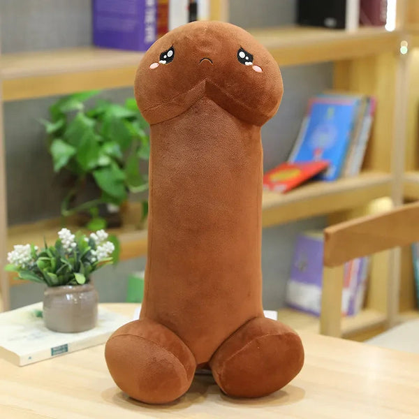 coussin en forme de penis rigolo qui a des yeux et une bouche. Ses pieds sont deux boules ce coussin est posé sur une table en bois