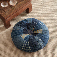 coussin de méditation capitoné au centre avec de nombreux motifs bleu il est posé sur un sol tissé une table basse est situé en haut a gauche de l'image