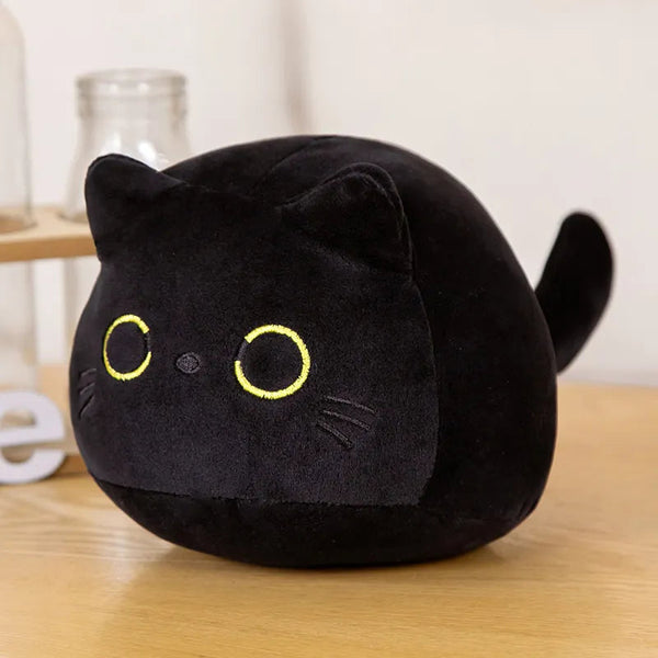 Coussin en forme de ballon qui représente un chat noir avec des yeux jaune et une petite queu. Il est posé sur une table en bois