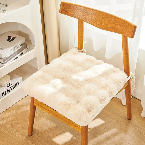 Coussin de chaise en fausse fourrure blanc attaché sur une chaise en bois posé en intérieur sur un parquet