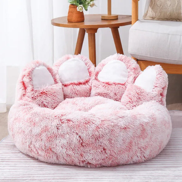 Coussin pour chien xxl en forme de pate le coussin est rose il est posé au sol sur un tapis avec un tabouret en arrière plan 