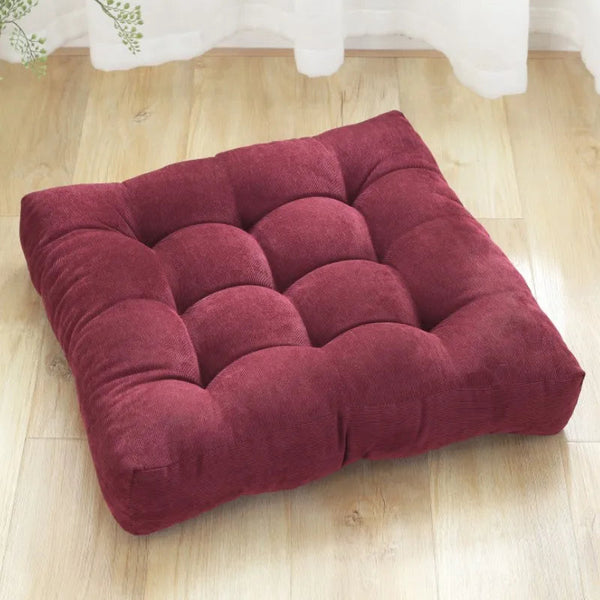 Coussin capitonné carré bordeaux posé sur le parquet