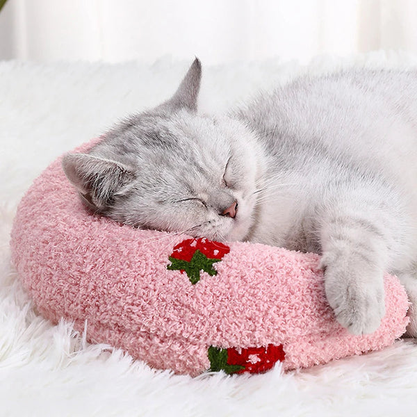 coussin pour chat en demi lune rose avec des motifs de fraise rouge et verte brodées  un chat dort paisiblement sur le coussin