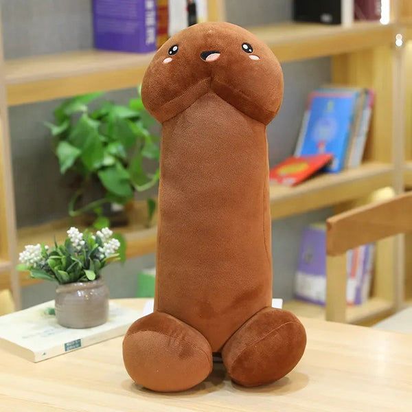 coussin en forme de penis rigolo qui a des yeux et une bouche. Ses pieds sont deux boules ce coussin est posé sur une table en bois