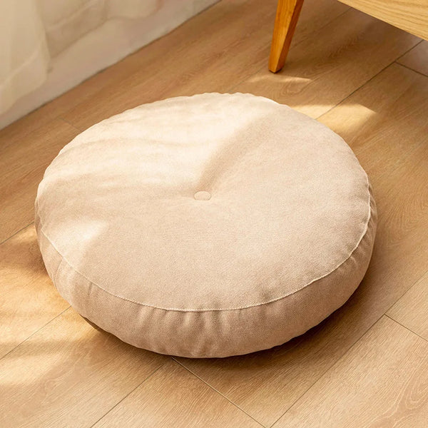 Coussin de sol rond beige en tissu, posé sur un sol en bois clair, apportant douceur et confort à votre intérieur.